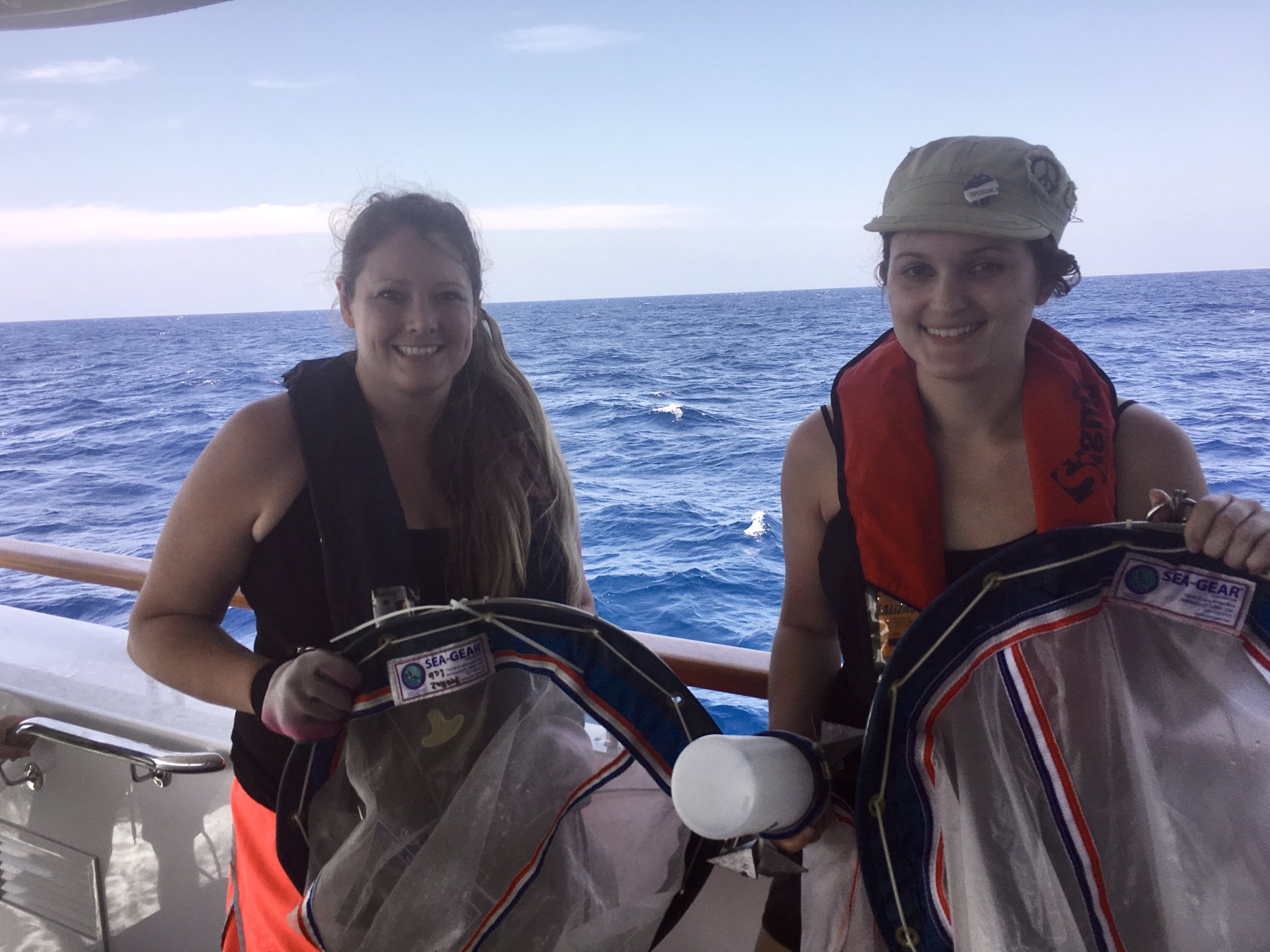 Gabrielle and Emily Dabe on deck holding plankton nets, open ocean behind them