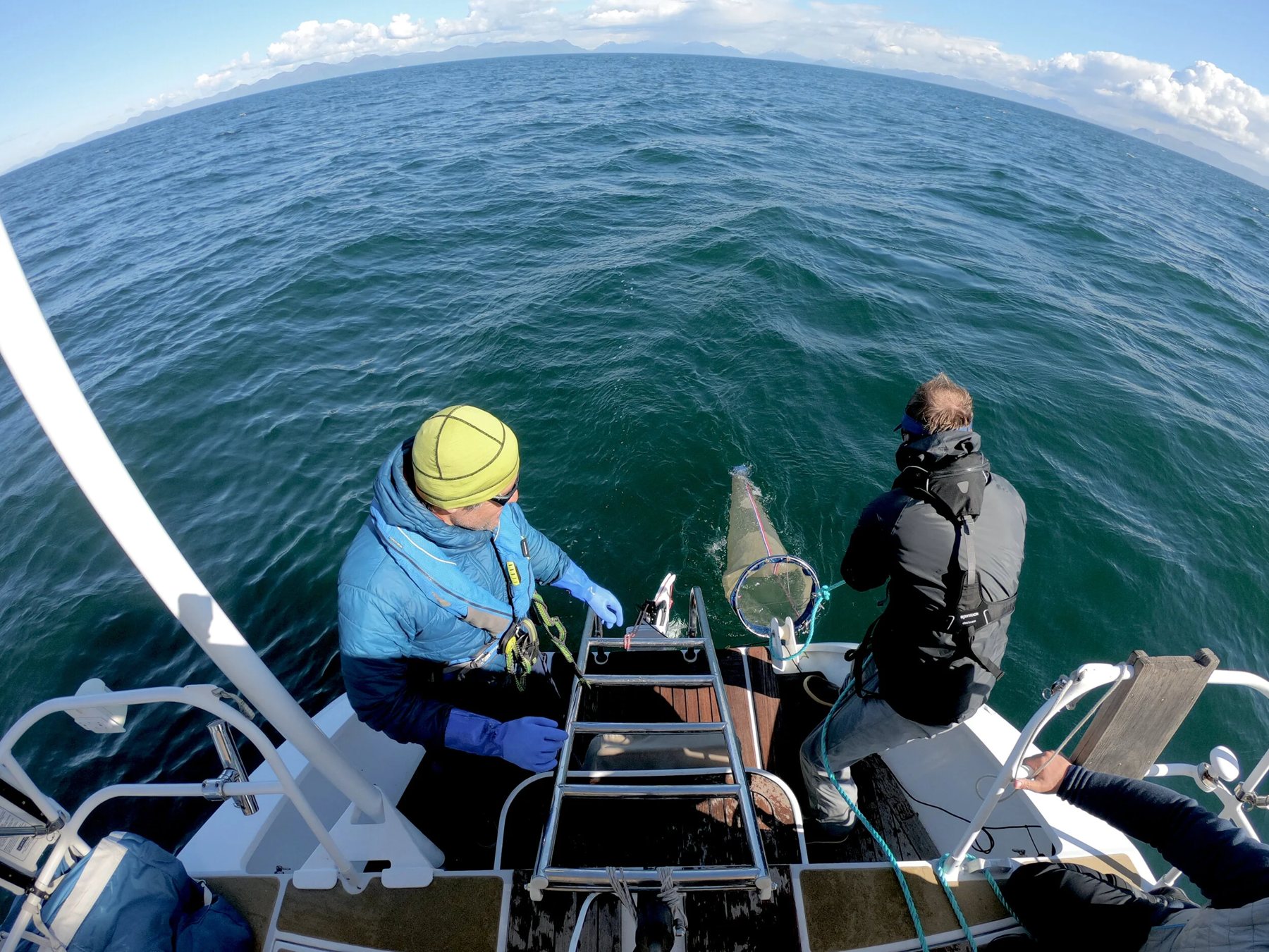 Two people sampling from the deck of a research vessel in Shelikof Strait